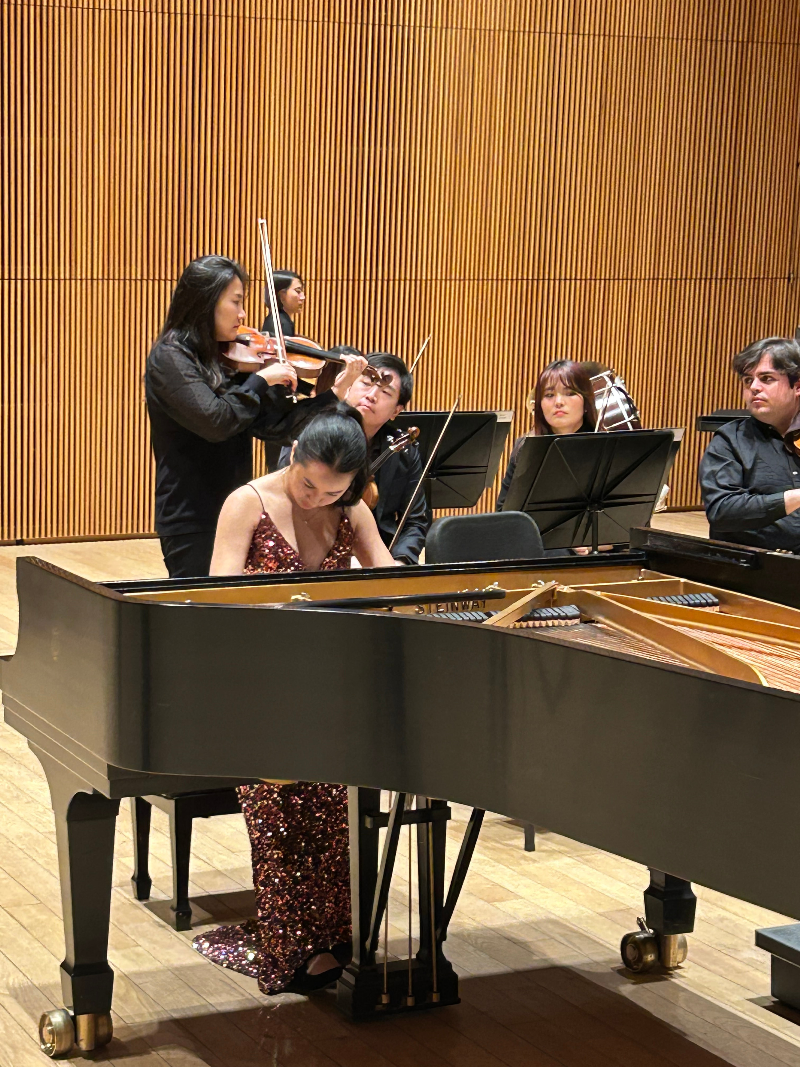 Leah Gavilan at the open piano with string players, in a burgundy gown.