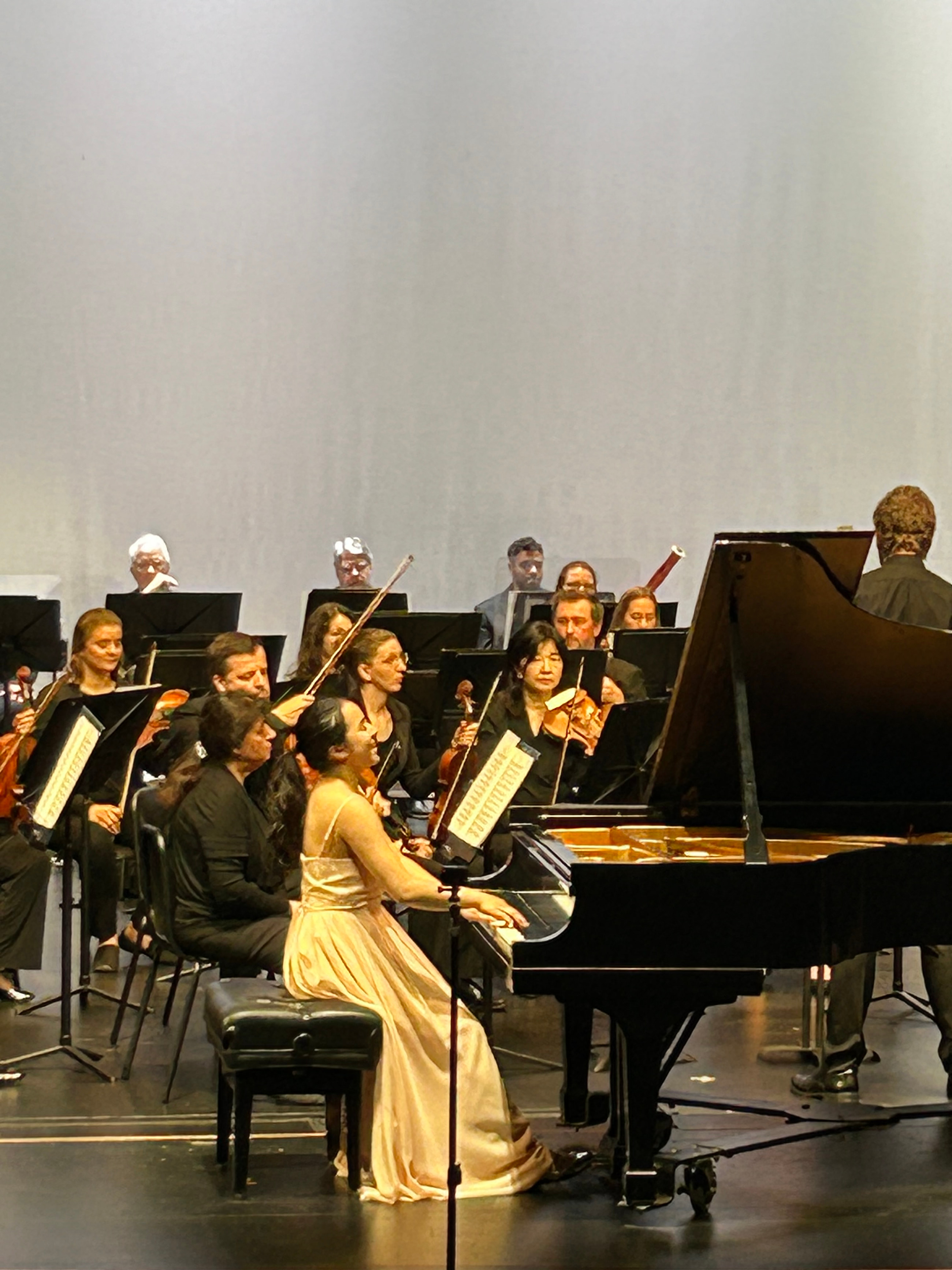 Leah Gavilan at the piano with orchestra, in a pale gold gown.