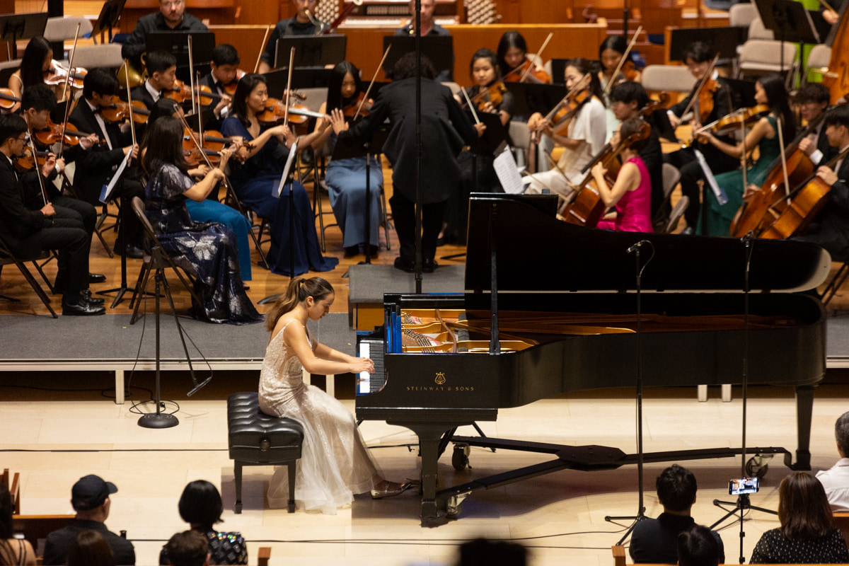 Leah Gavilan performing a concerto, seen from above with the full orchestra and audience.