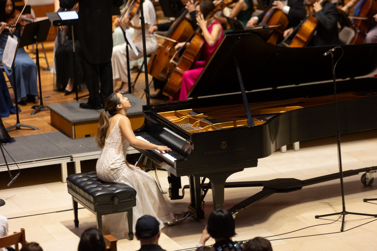 Leah Gavilan in profile at the keyboard, orchestra behind her.